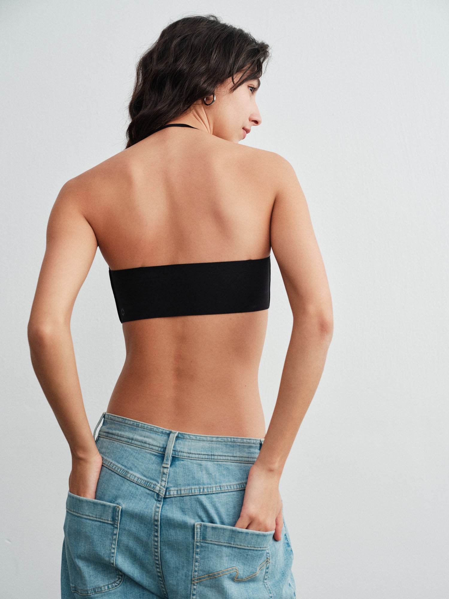 Model wearing a black strapless top and blue jeans on a light gray background. 