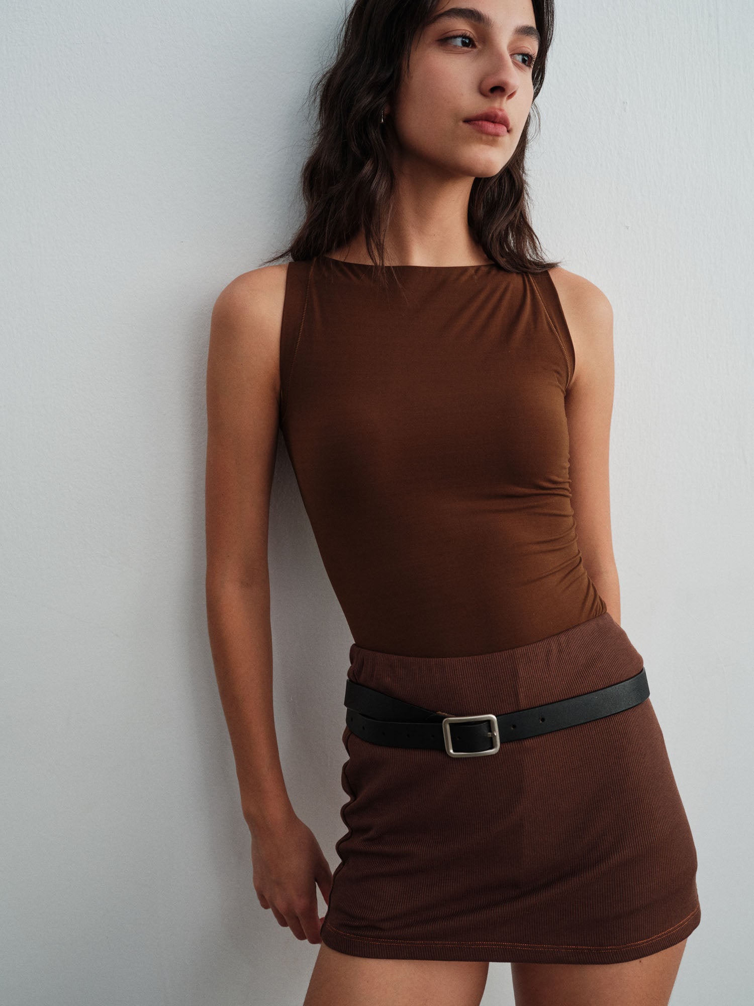 Model wearing a brown top with a skirt and belt against a plain background.
