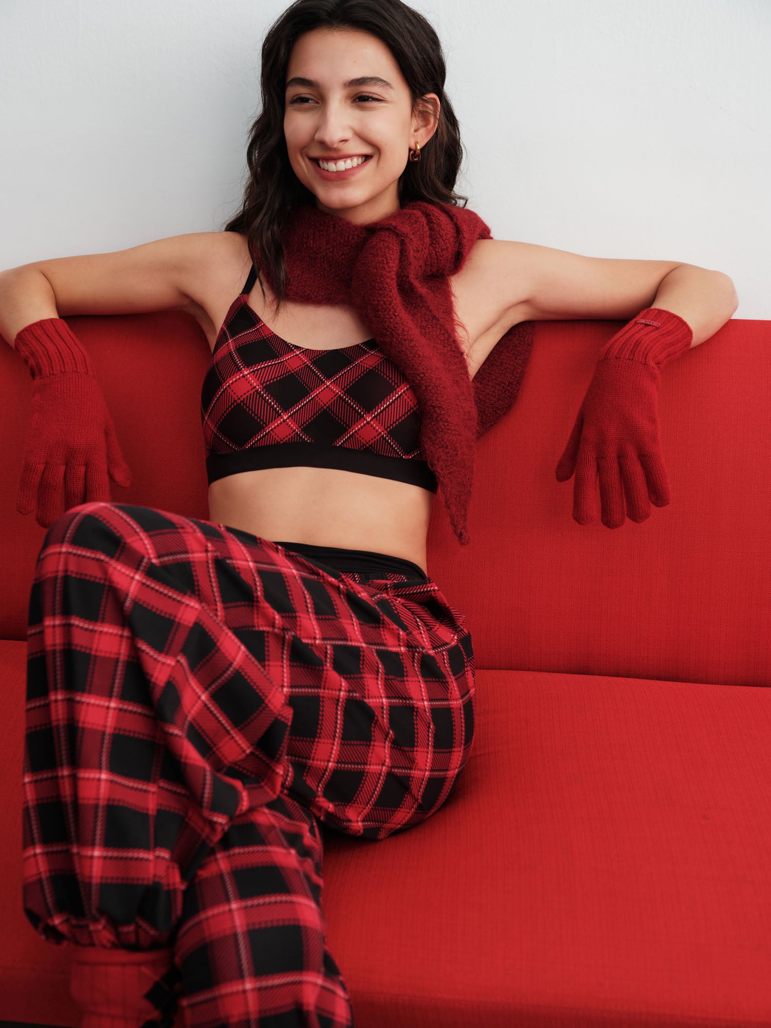 Woman wearing a red and black plaid outfit with gloves and a scarf, sitting on a red couch.