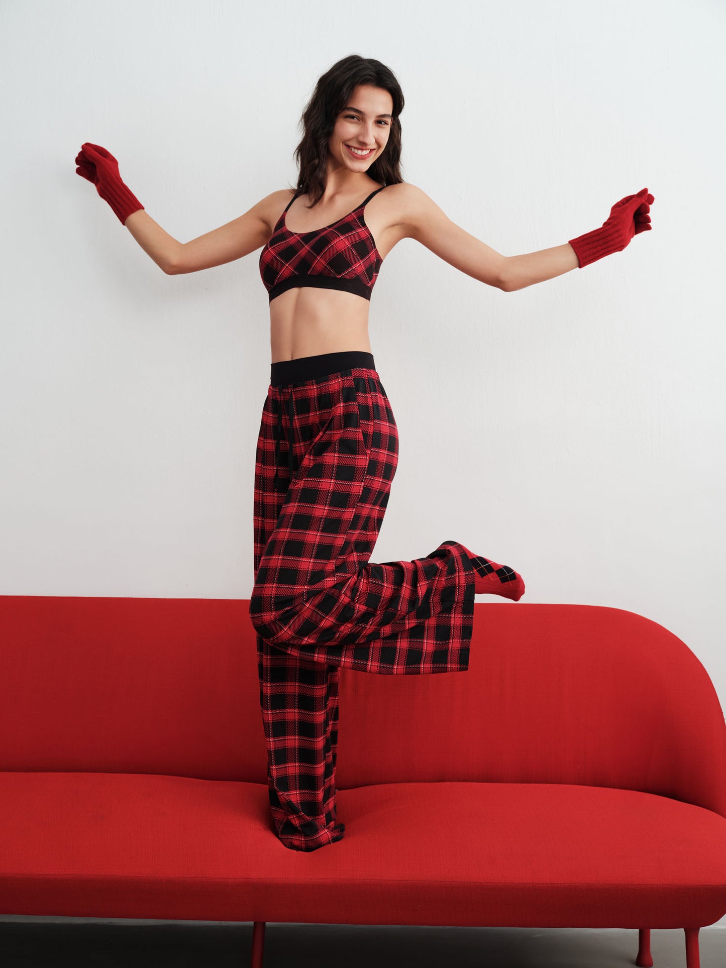 Woman in red and black checkered outfit standing on a red couch against a white background.