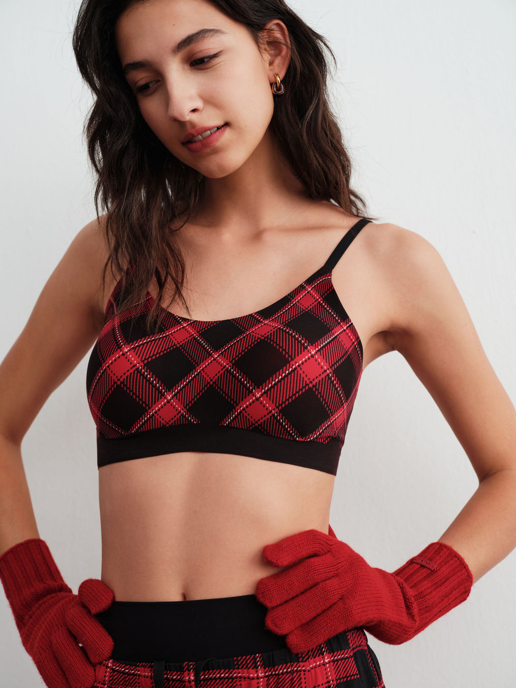 Woman wearing a red and black plaid bra and leggings with red gloves on a white background.