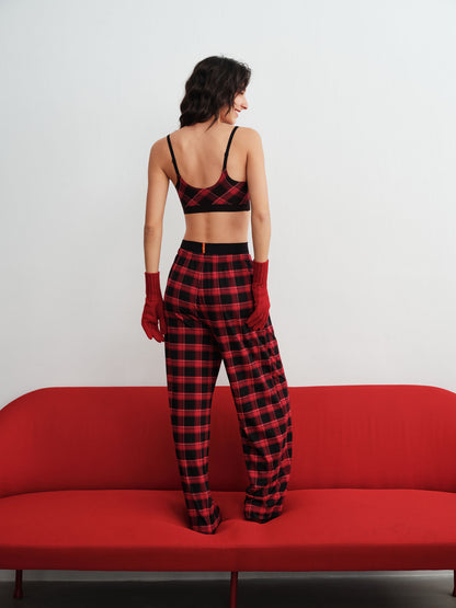 Woman wearing a red and black checkered outfit standing on a red couch against a white background.