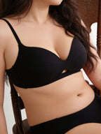 Person wearing a black bra and underwear set with a neutral background. Black