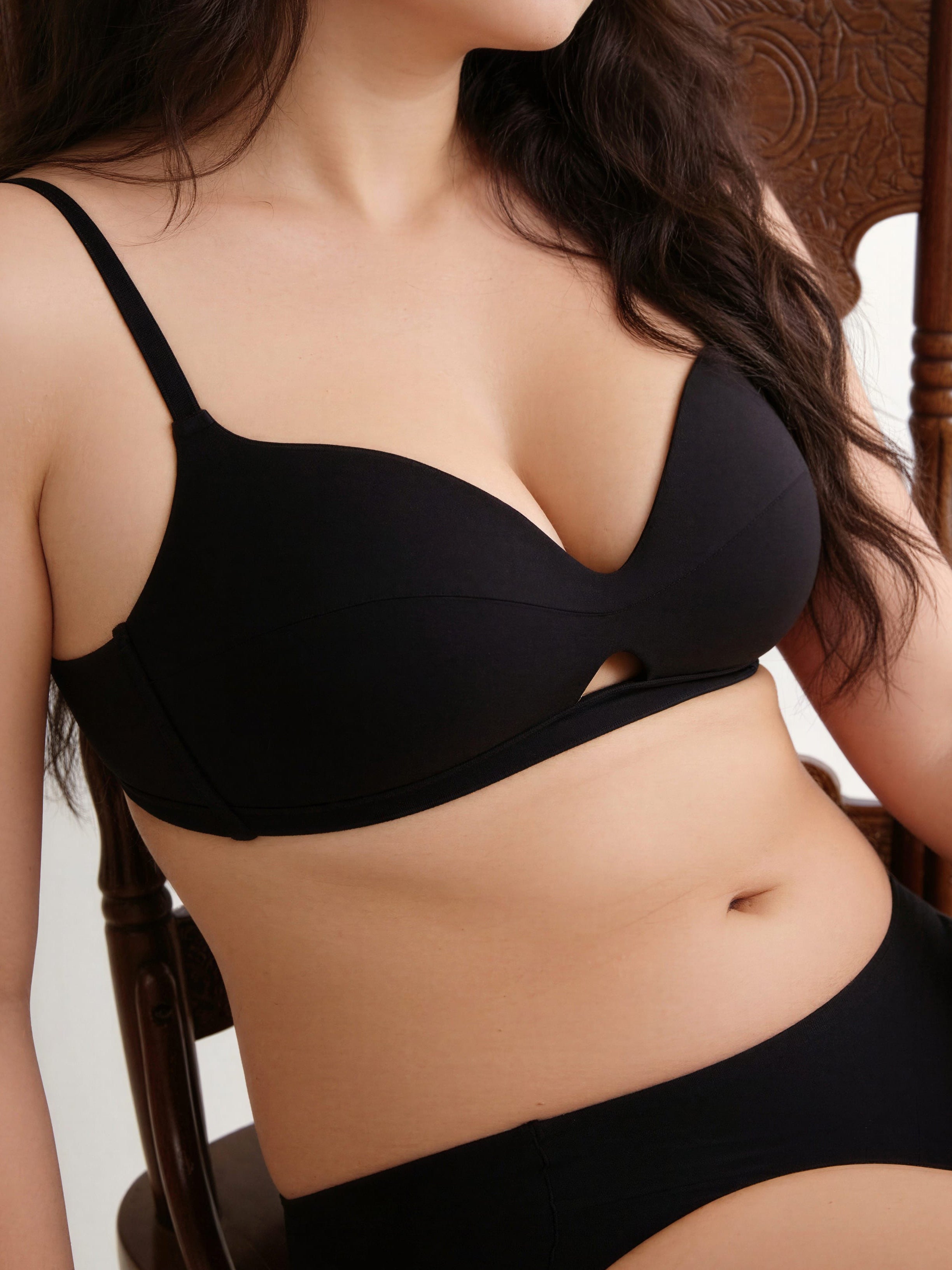 Person wearing a black bra and underwear set with a neutral background. Black