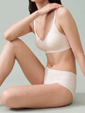 A woman wearing a light beige wireless bra and matching high-waisted briefs, posing against a solid light gray background. eggwhite