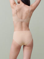 Rear view of a model wearing a nude-beige seamless bra and matching high-waisted briefs against a solid sage green background. peach pure