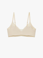 A light beige wireless bra with thin adjustable shoulder straps, displayed against a clean, solid off-white background. Eggwhite