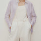 a short curly hair woman wearing a light purple shirt. w white camisole under the shirt and a white pants. 