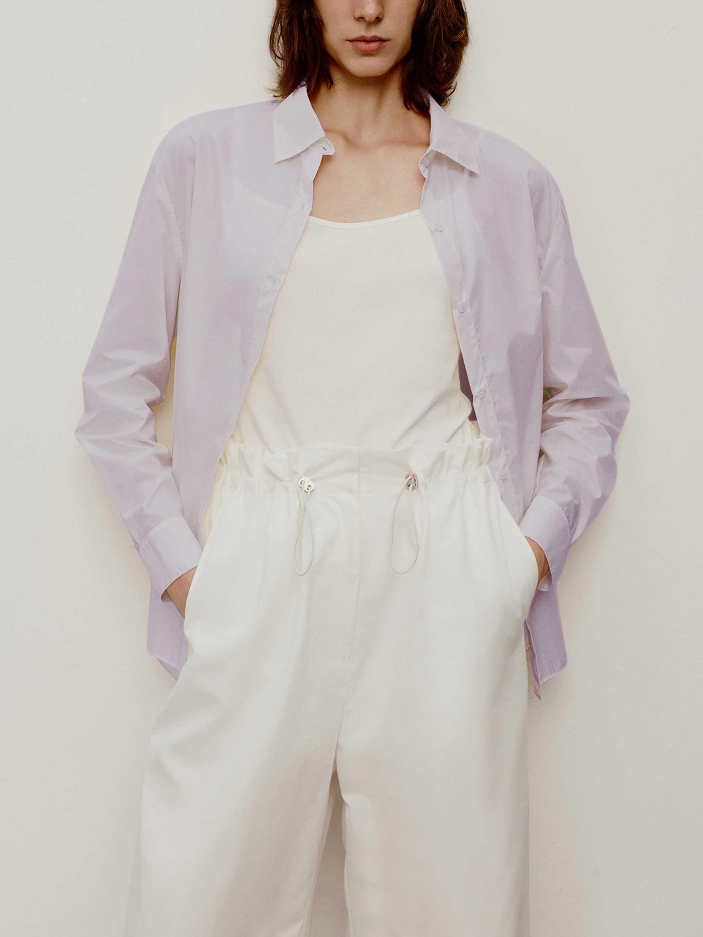 a short curly hair woman wearing a light purple shirt. w white camisole under the shirt and a white pants. 