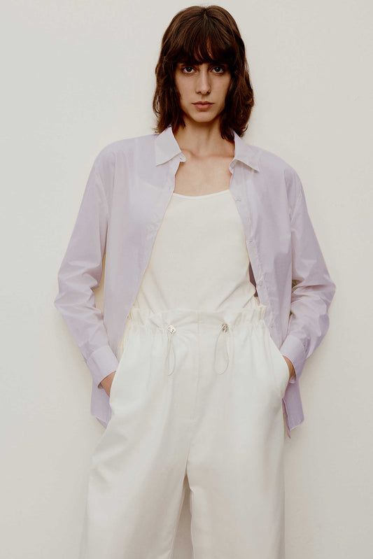 a short curly hair woman wearing a light purple shirt. w white camisole under the shirt and a white pants. 