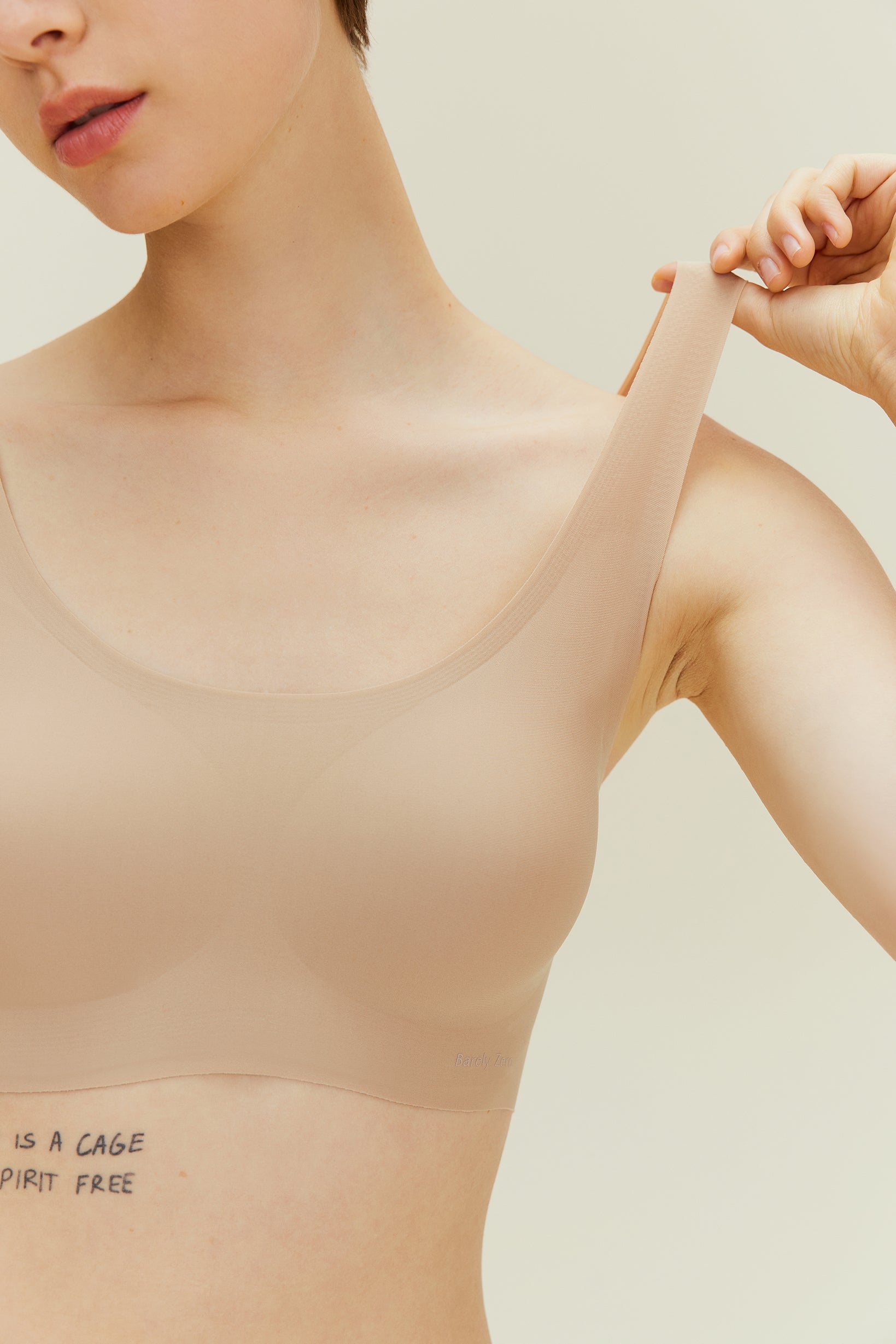 Woman wearing a beige bralette against a neutral background