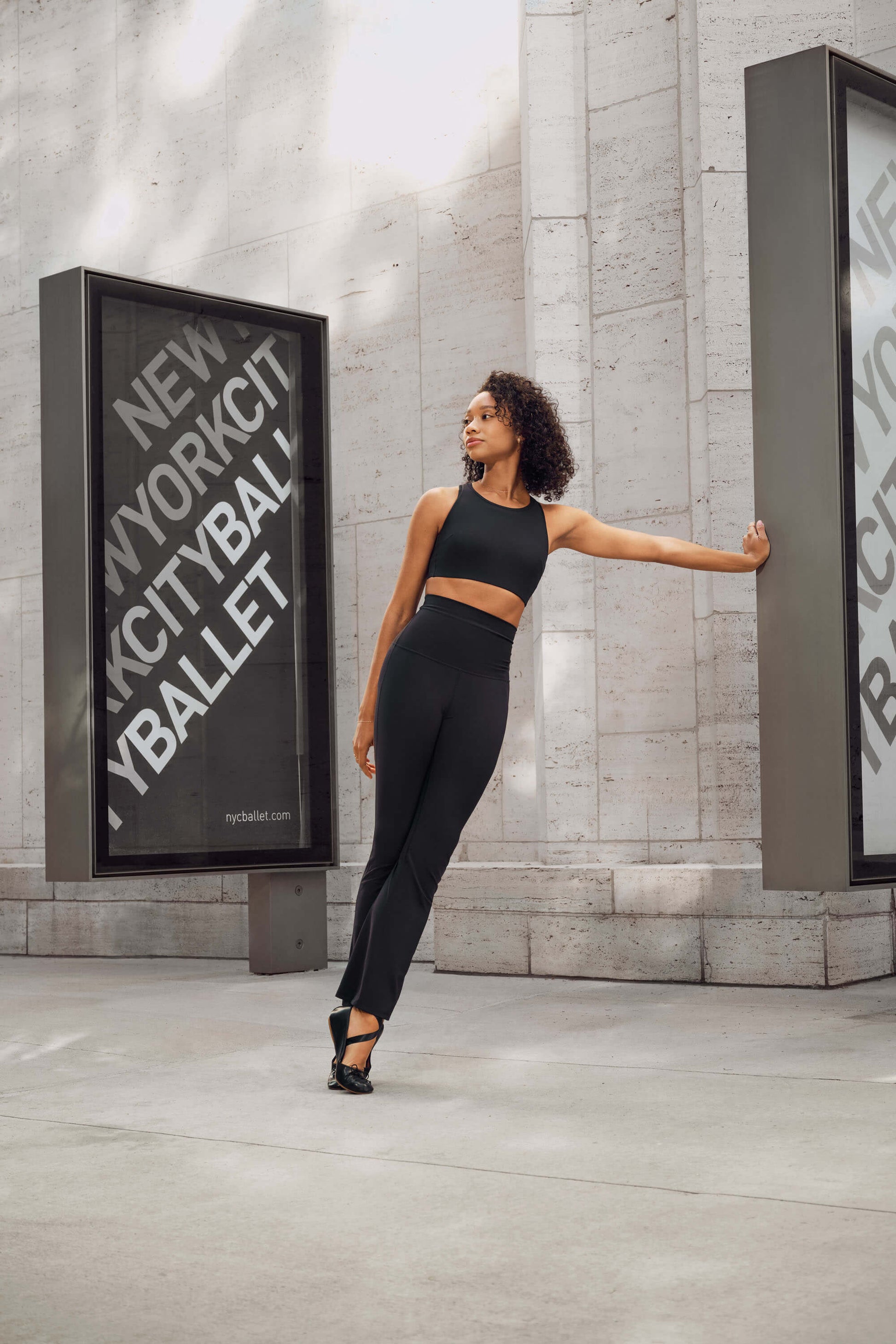 Dancer leaning against billboard wearing black tank top and black flare leggings