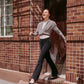 Dancer stepping from doorway wearing gray wrap sweater, white tank top, and black legging pants