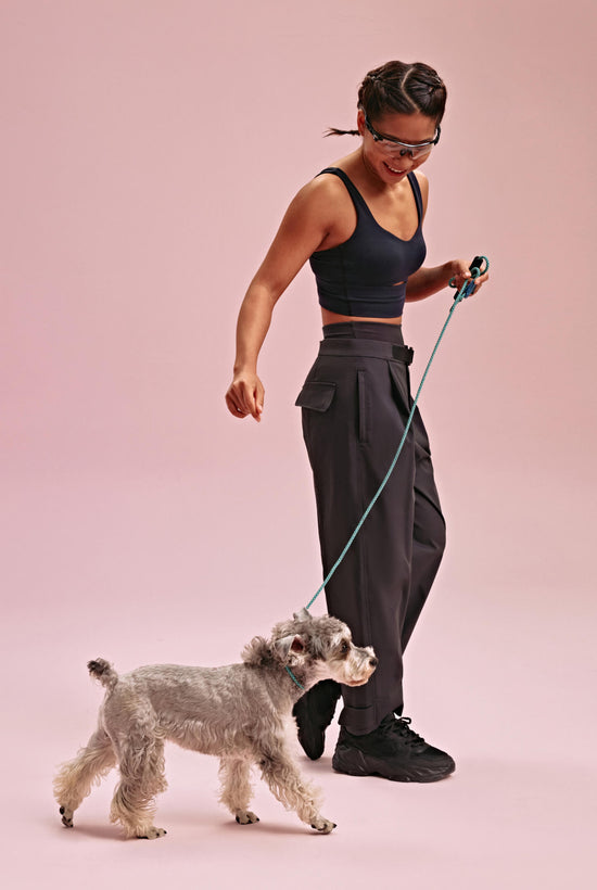 Woman wearing black sports bra and black pants walking a gray dog