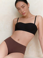 Woman wearing a black bikini top and brown bottoms against a neutral background. Brown color.