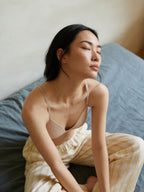 Woman wearing a beige bra and yellow pants sitting on a bed.
