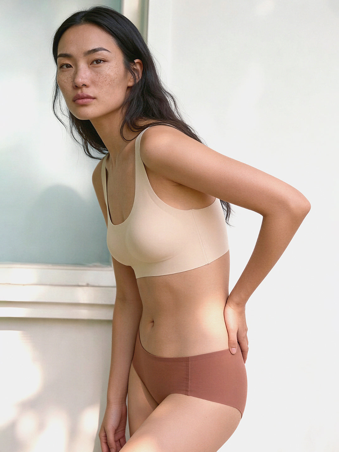 Woman wearing beige tank top and brown underwear against a light background