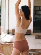 Person wearing a white bra and pink underwear in a room with large windows.