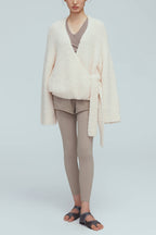 a woman wearing a white wool wrap cardigan and light grey leggings. 