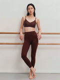 Woman wearing a brown sports bra and leggings standing against a plain background