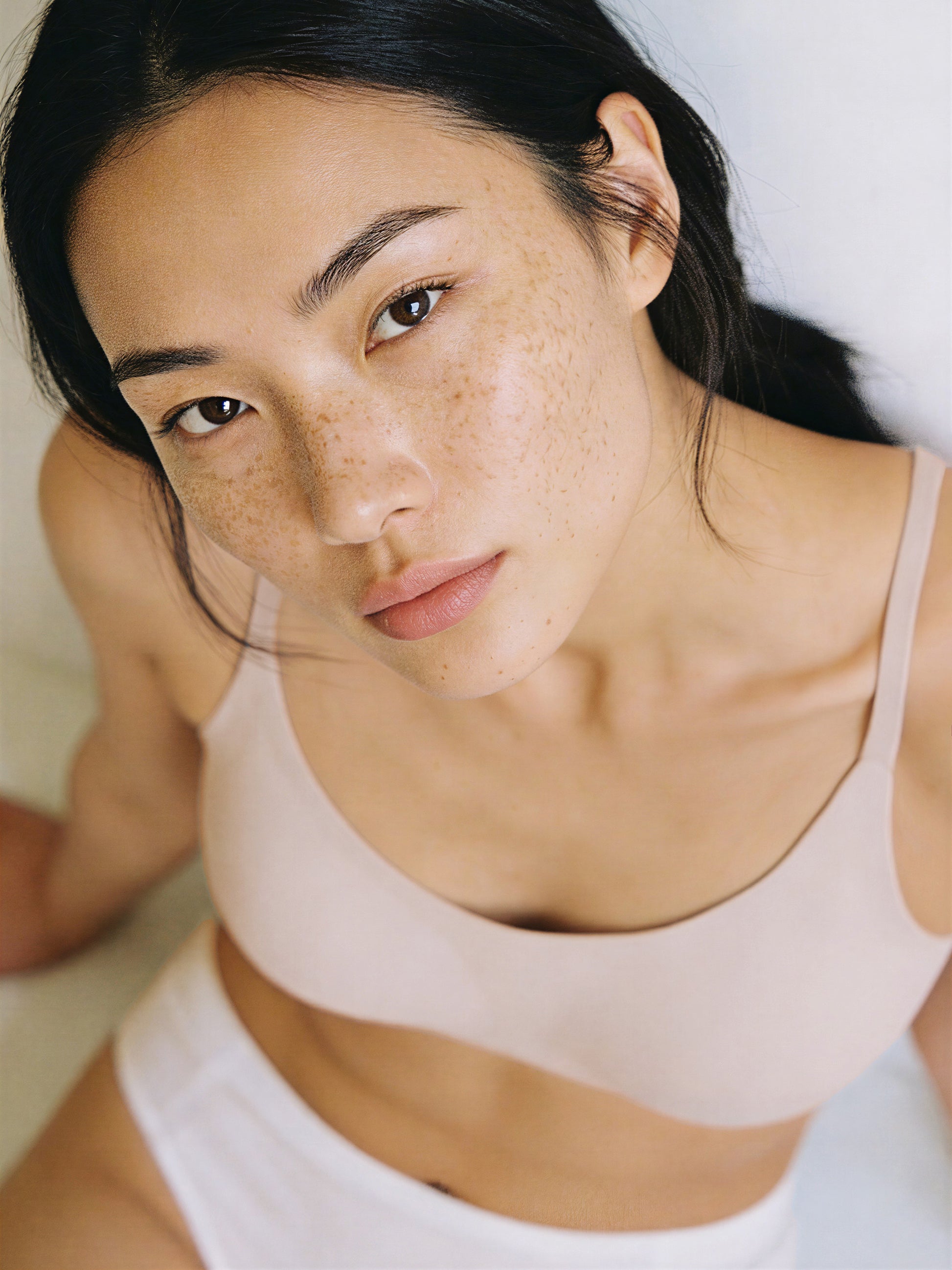 Woman wearing a beige tank top with a plain background