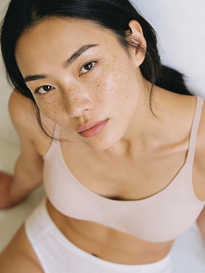 Woman wearing a beige tank top with a plain background