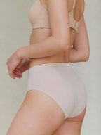 Model wearing a beige bra and high-waisted underwear on a plain background. Fluffy Peach color.