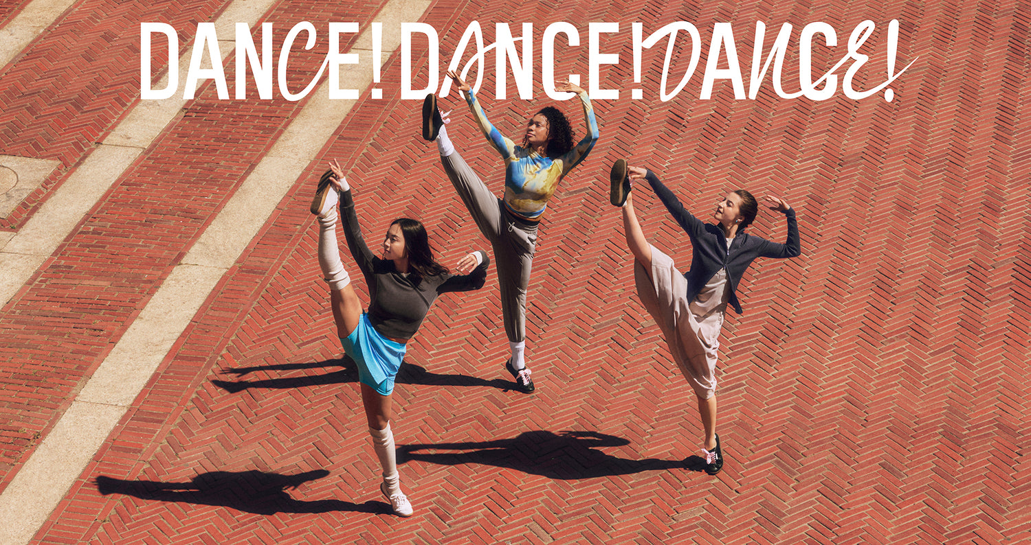 Three dancers kicking into the sky. One on left wears dark gray sweatshirt, blue skort, and gray leg warmers. One in middle wears blue and brown print shirt and gray pants. One on right wears gray dress and dark gray zip cardigan. Dance! Dance! Dance! is written on top of image