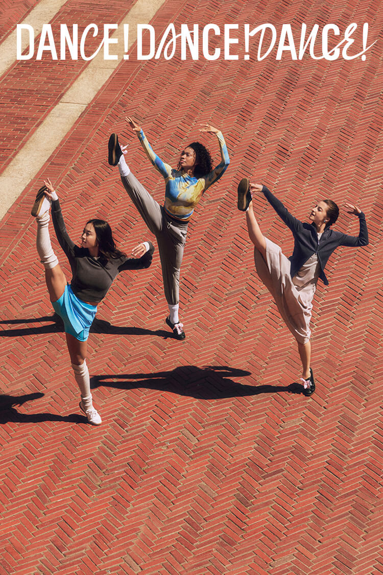 Three dancers kicking into the sky. One on left wears dark gray sweatshirt, blue skort, and gray leg warmers. One in middle wears blue and brown print shirt and gray pants. One on right wears gray dress and dark gray zip cardigan. Dance! Dance! Dance! is written on top of image