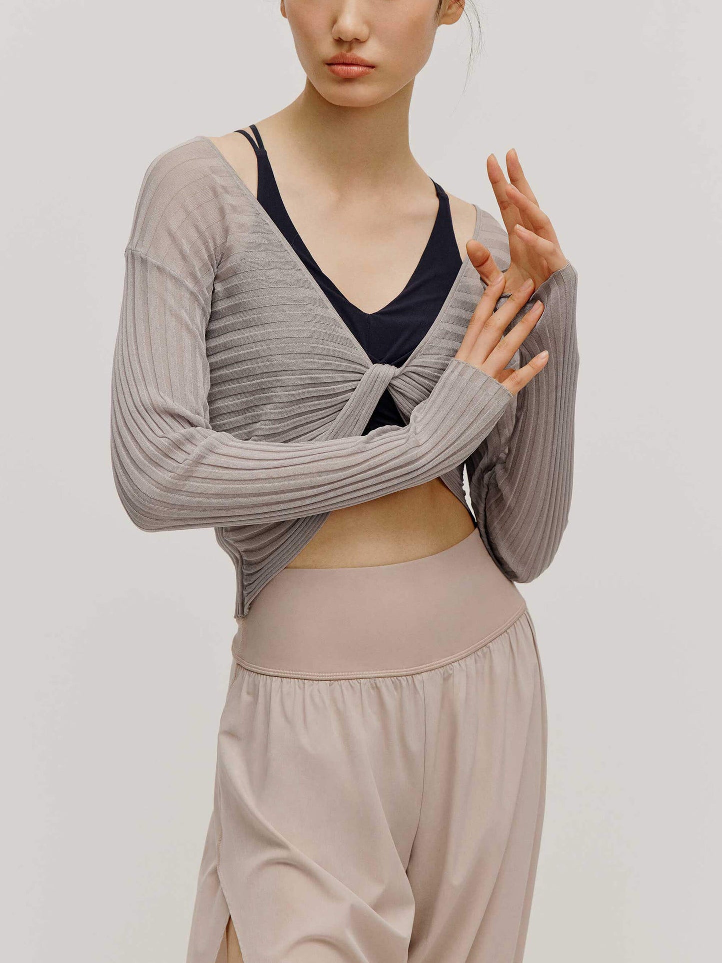 front view of a women wearing a neutral color woven jogger and a navy bra covered by a mauve color see thru knit top with a knot.