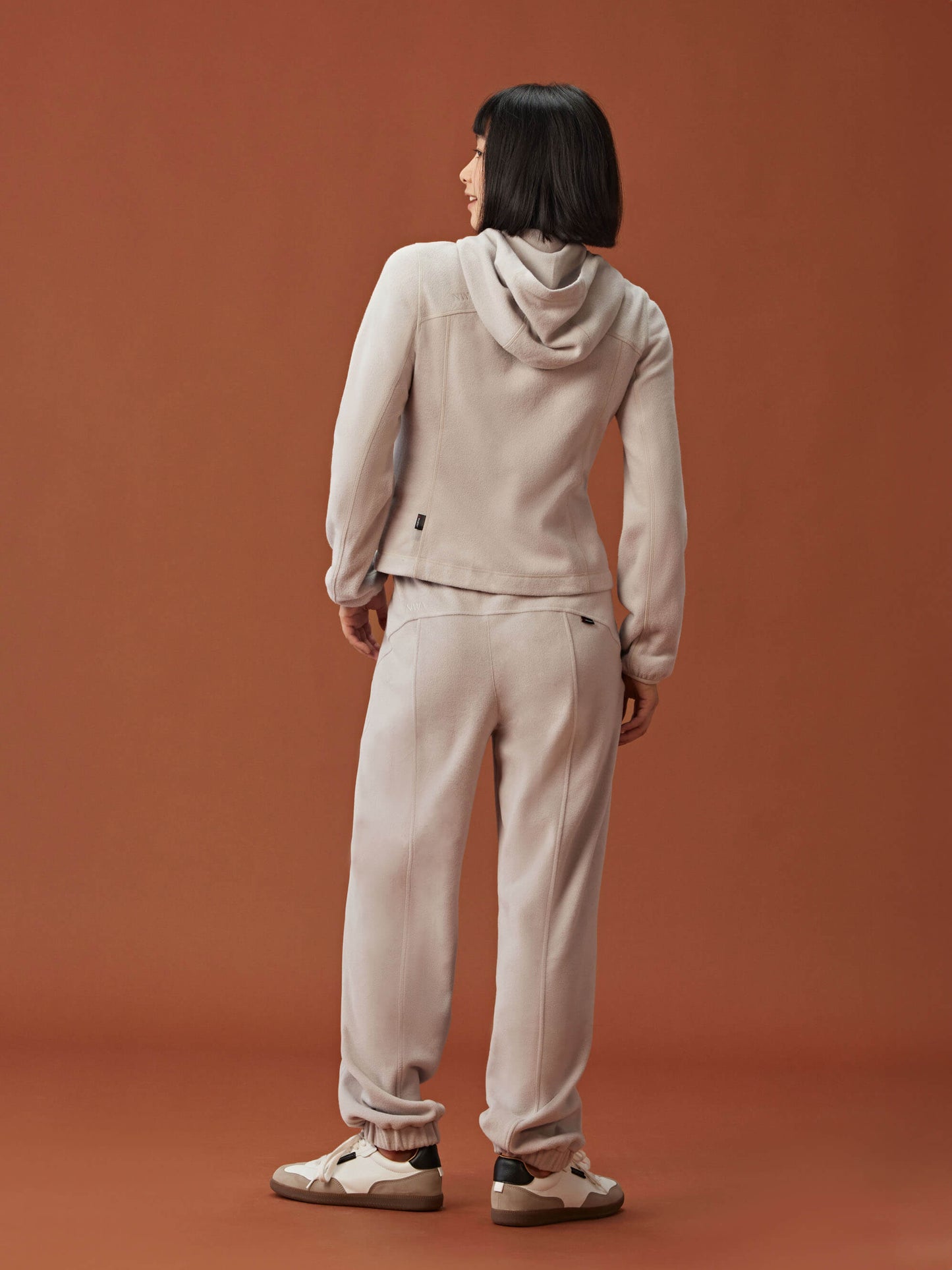 back of woman in beige zipped hooded fleece jacket and matching pants.