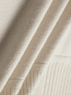 Close-up of cream-colored fabric with a soft, ribbed texture, showing the material’s weave and softness. 