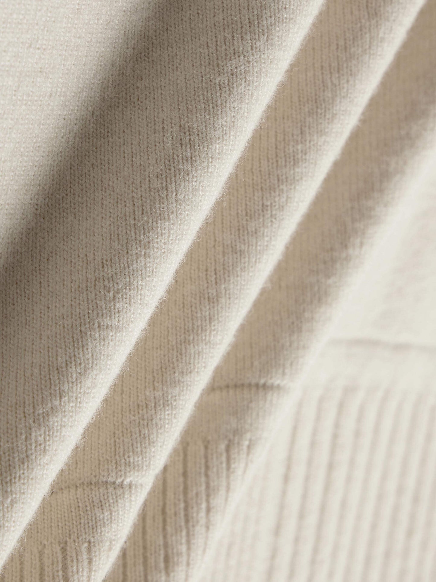 Close-up of cream-colored fabric with a soft, ribbed texture, showing the material’s weave and softness. 