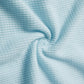 A close-up view of light blue waffle-knit fabric, showcasing its textured grid pattern and soft, stretchy material.