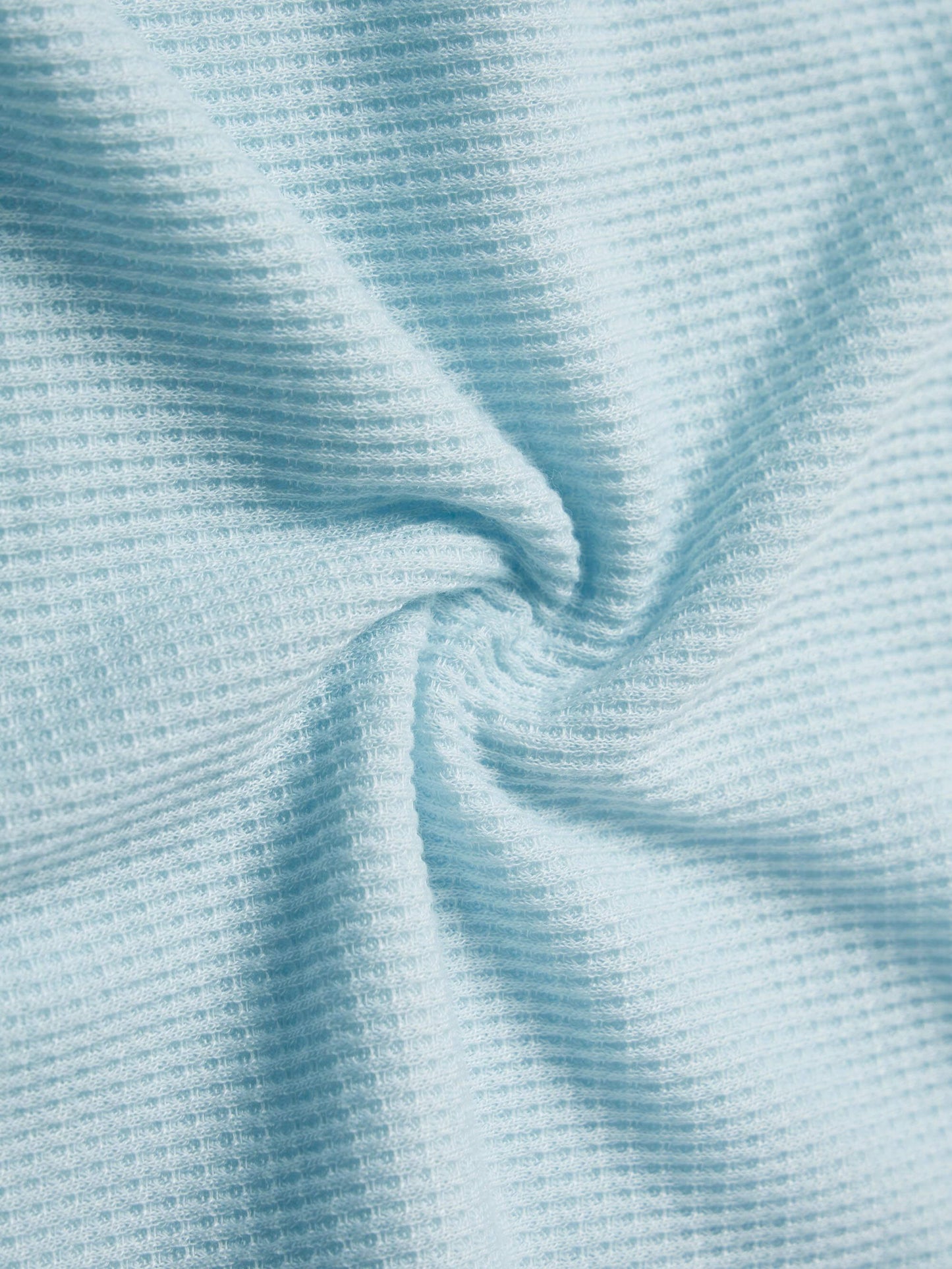 A close-up view of light blue waffle-knit fabric, showcasing its textured grid pattern and soft, stretchy material.