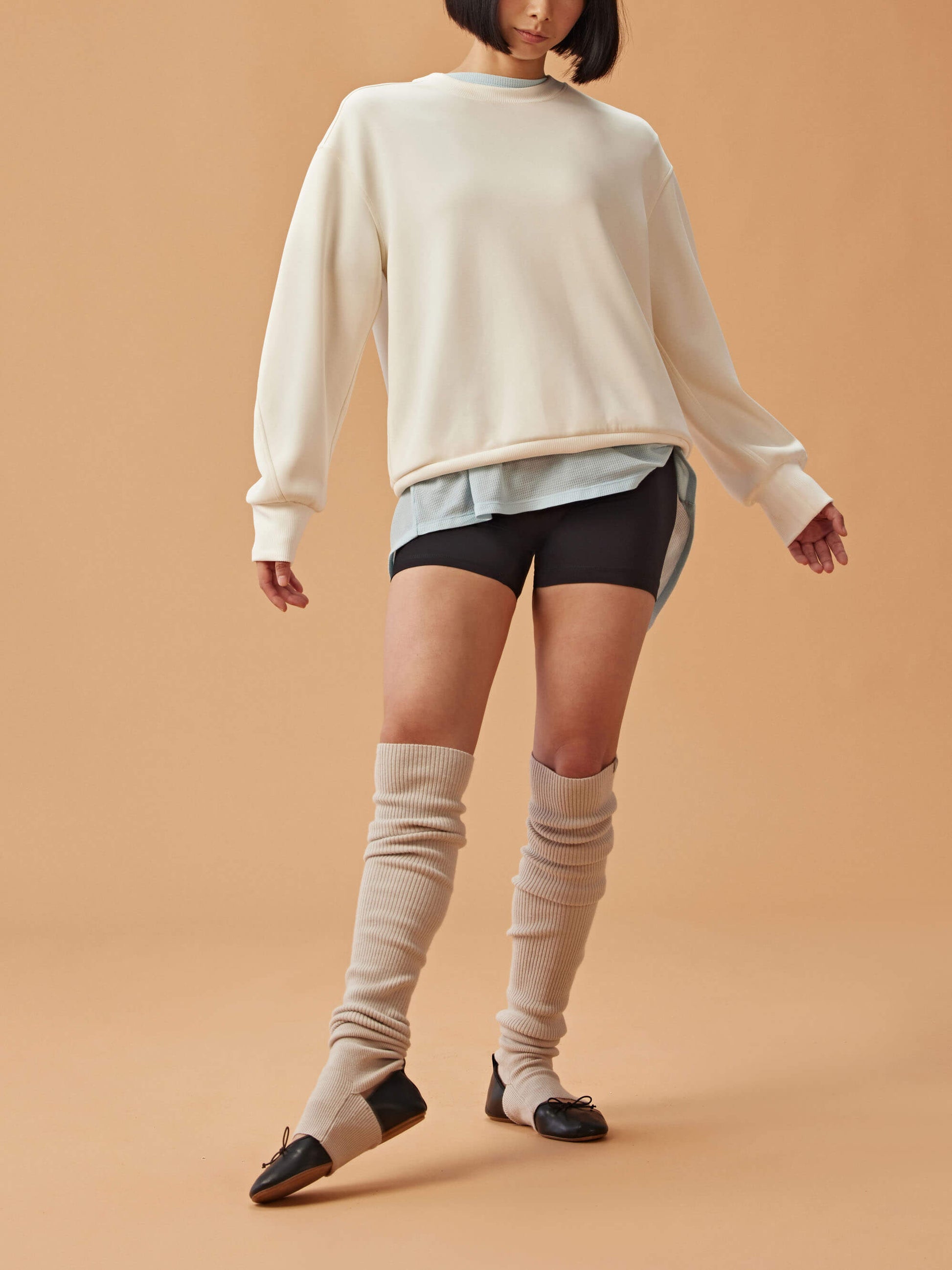 Woman wearing white sweatshirt and black shorts and gray leg warmers