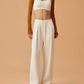 woman in white sports bra, mustard shrug and white wide leg pants