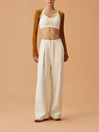 woman in white sports bra, mustard shrug and white wide leg pants