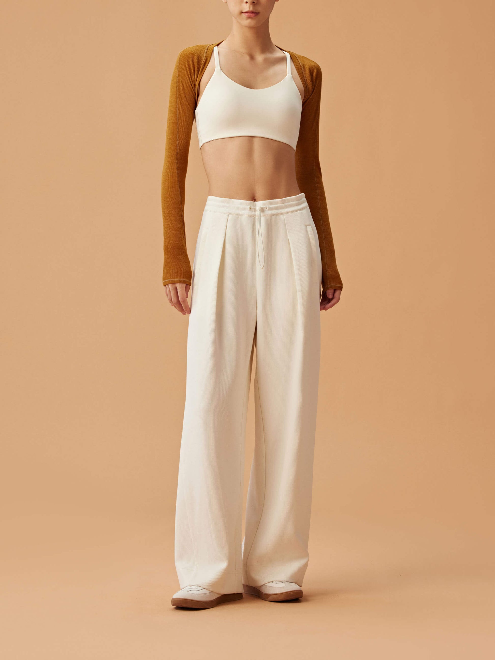 woman in white sports bra, mustard shrug and white wide leg pants