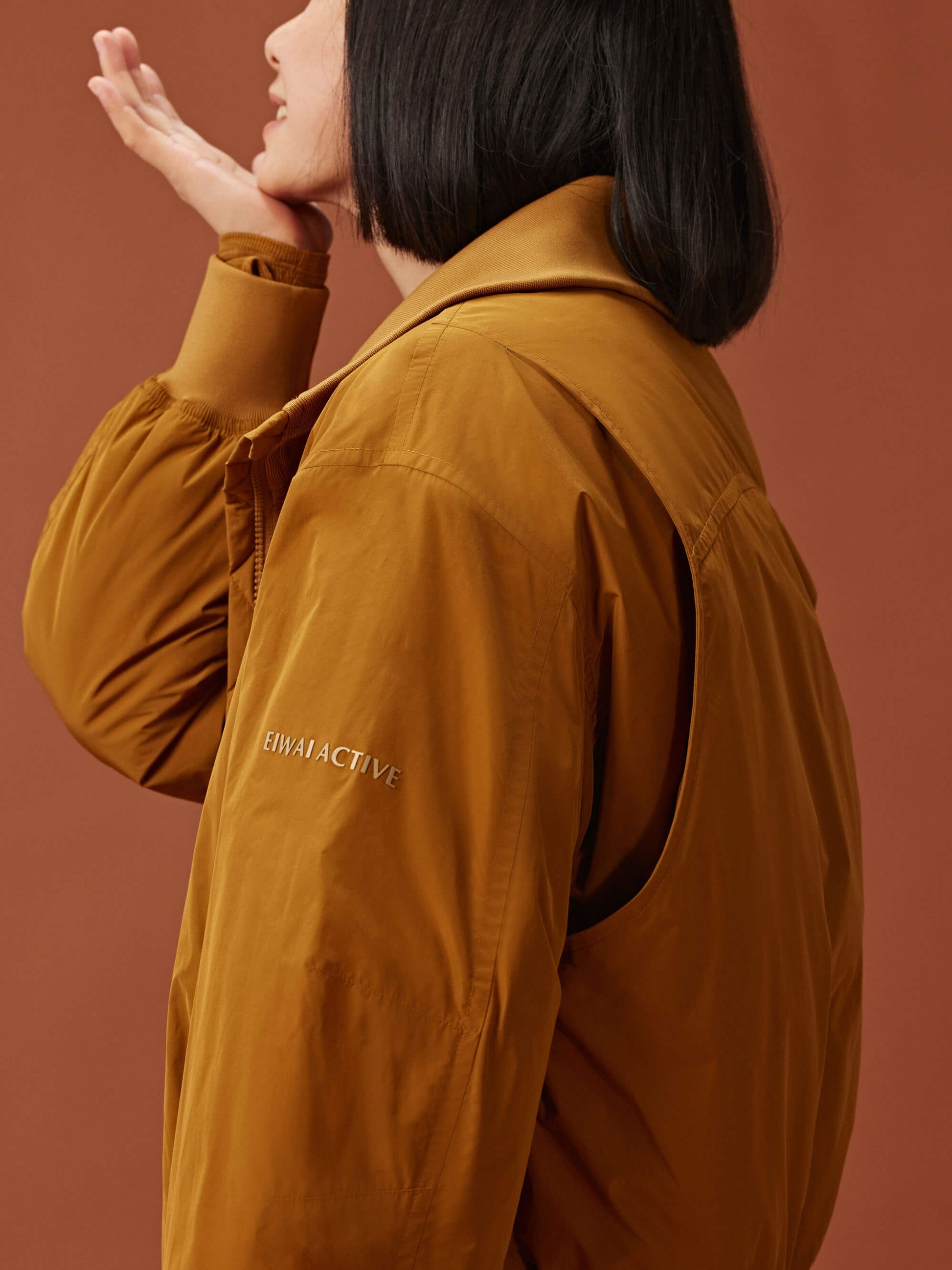 side of woman in a golden brown bomber jacket 