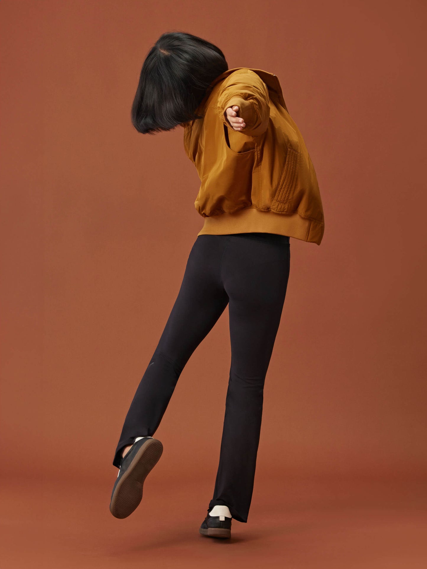 back of woman in a golden brown bomber jacket and black leggings