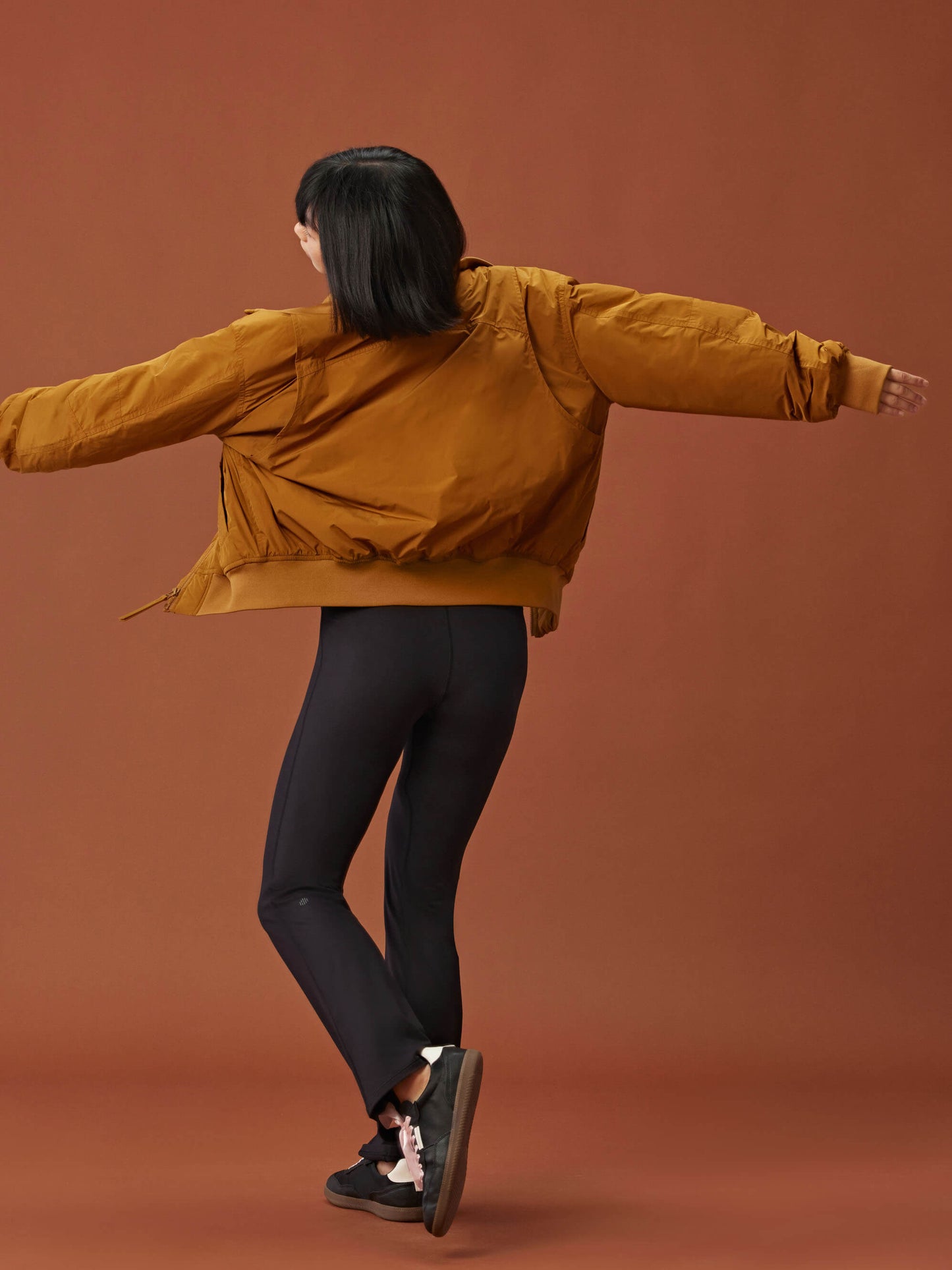 back of woman in a golden brown bomber jacket and black leggings