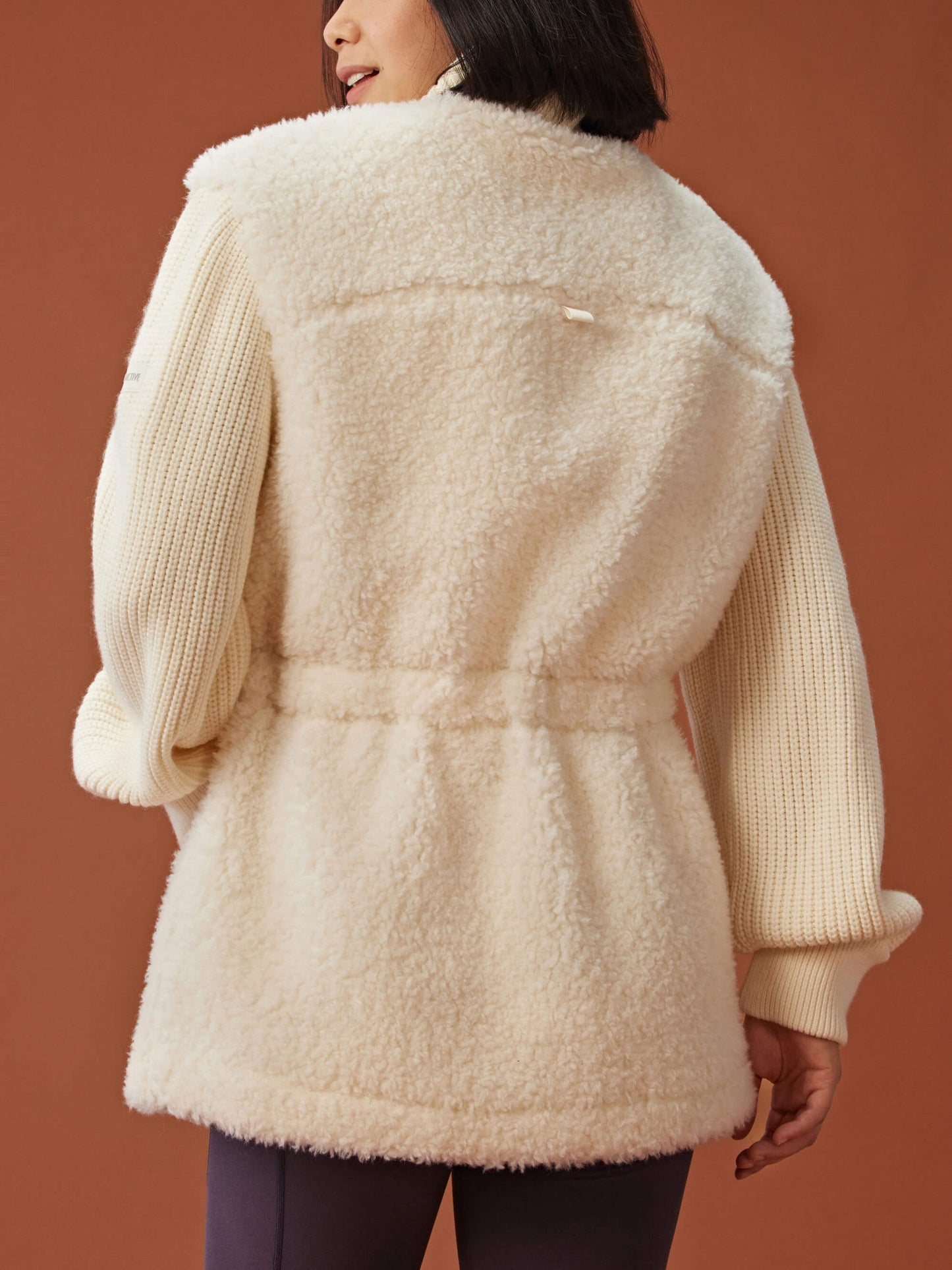 back of woman in white fleece coat with gathered waist and knitted sleeves