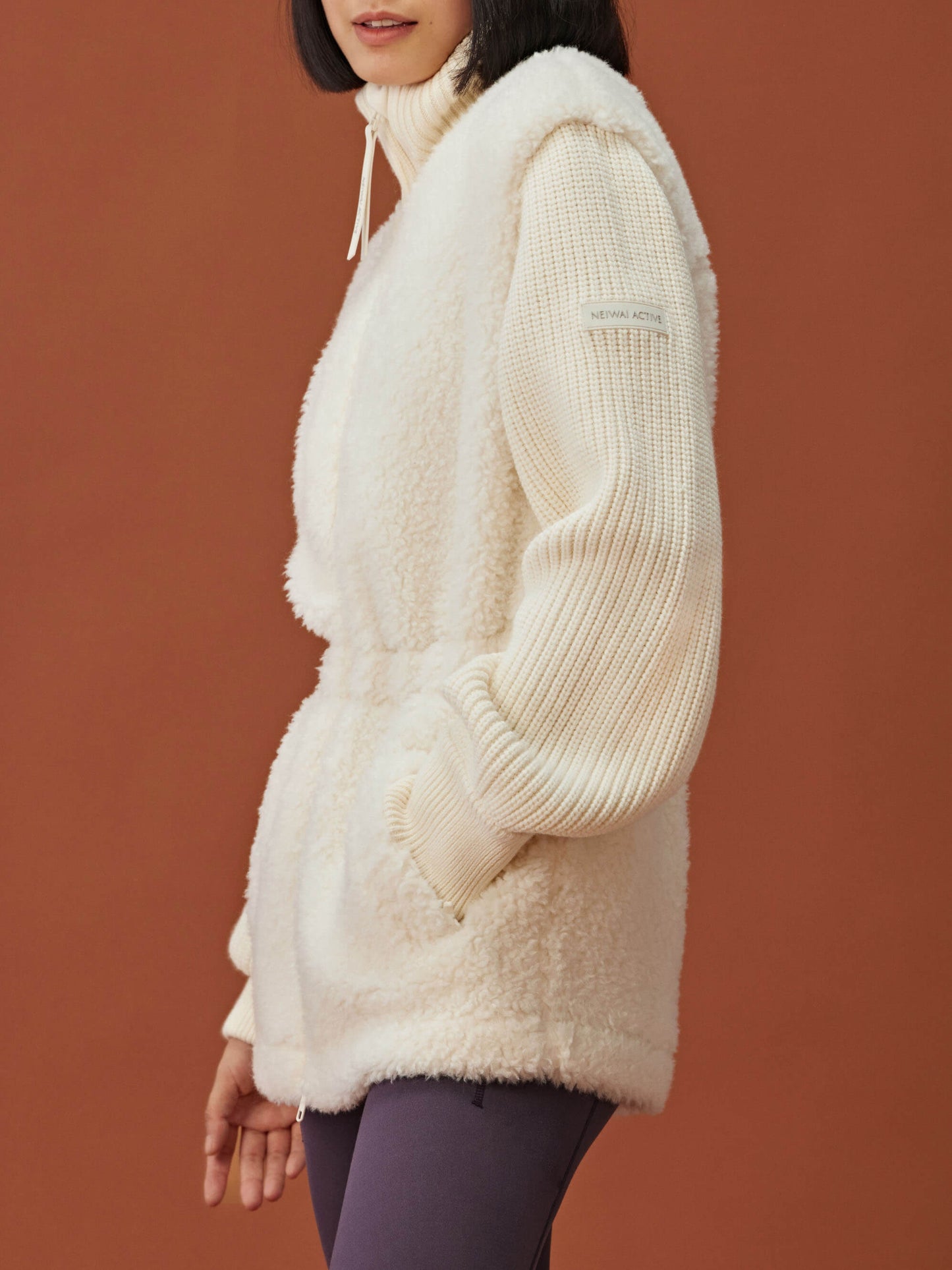 side of woman in white fleece coat with gathered waist and knitted sleeves