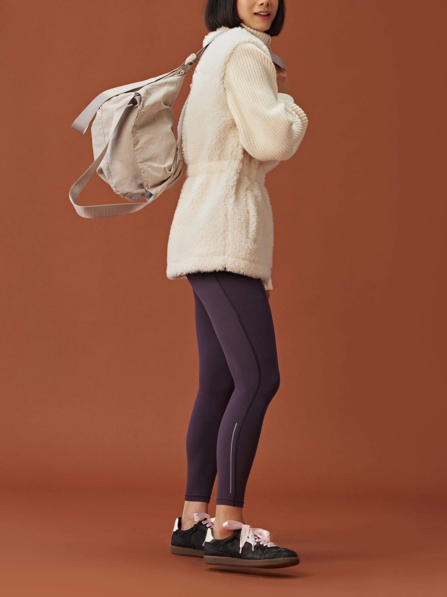 side of woman in white fleece coat with gathered waist and knitted sleeves and dark purple leggings