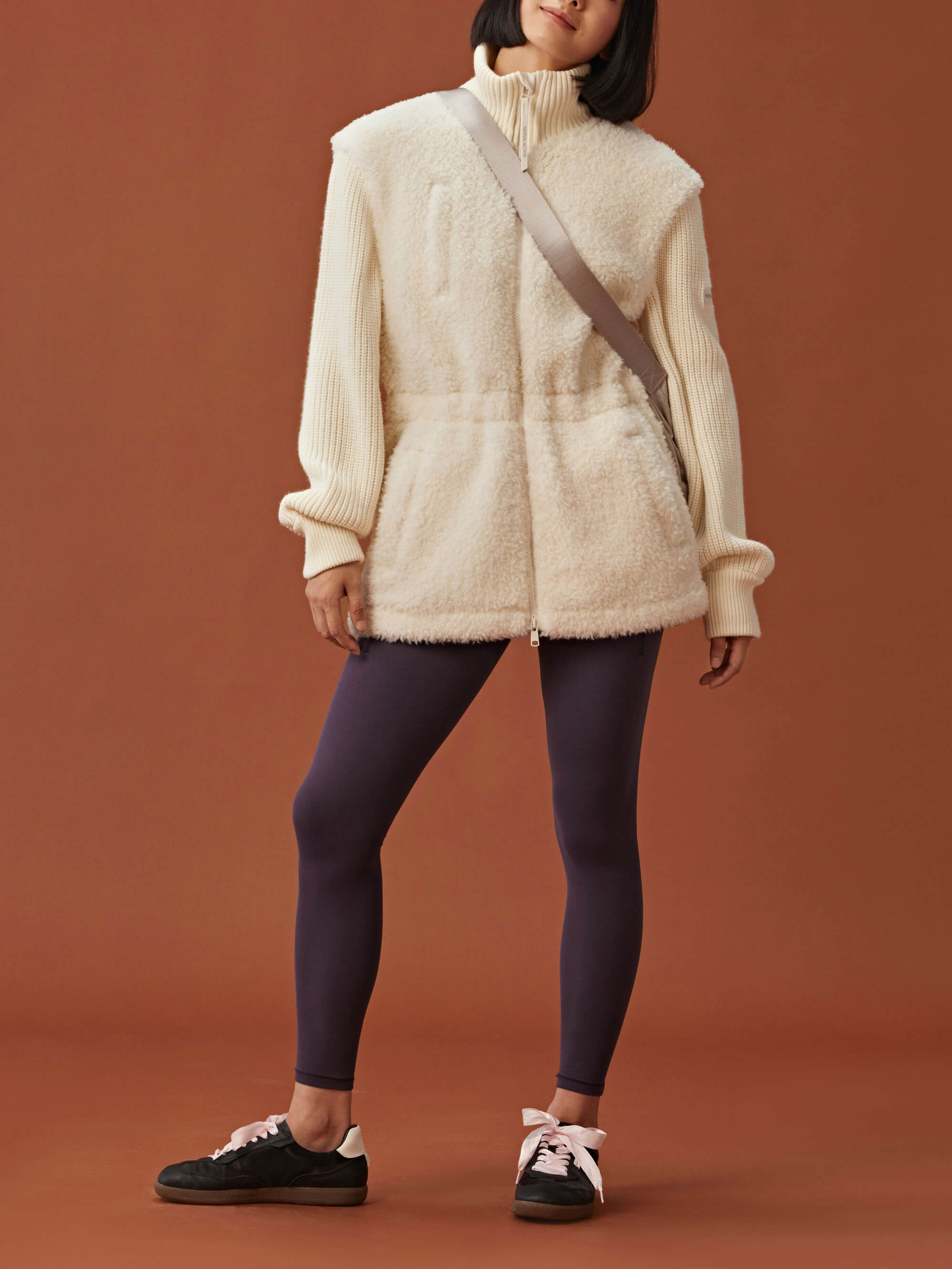 woman in white fleece coat with gathered waist and knitted sleeves and dark purple leggings
