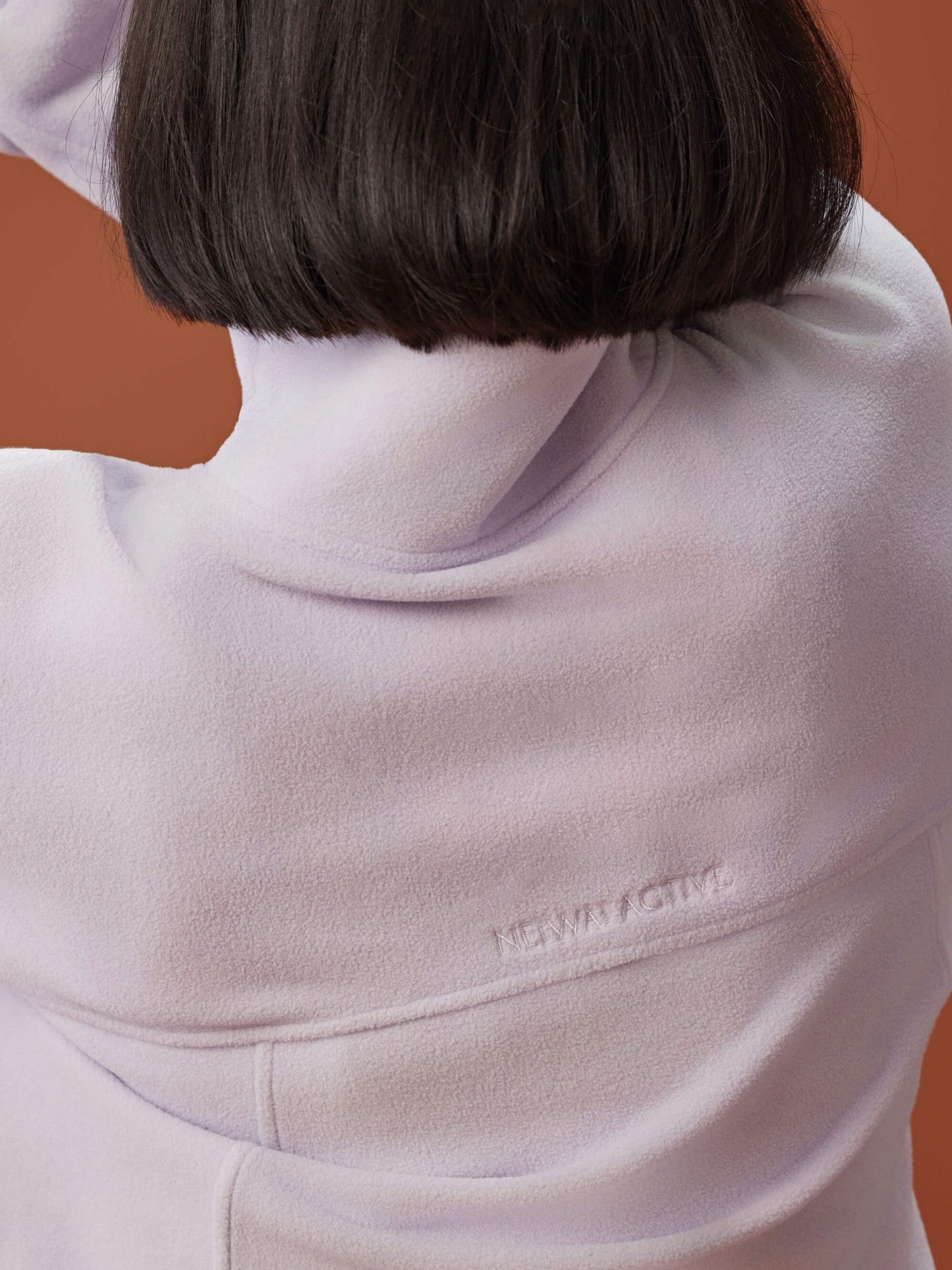 back of woman in light purple fleece sweatshirt, showcasing the NEIWAI ACTIVE stitch on the back.