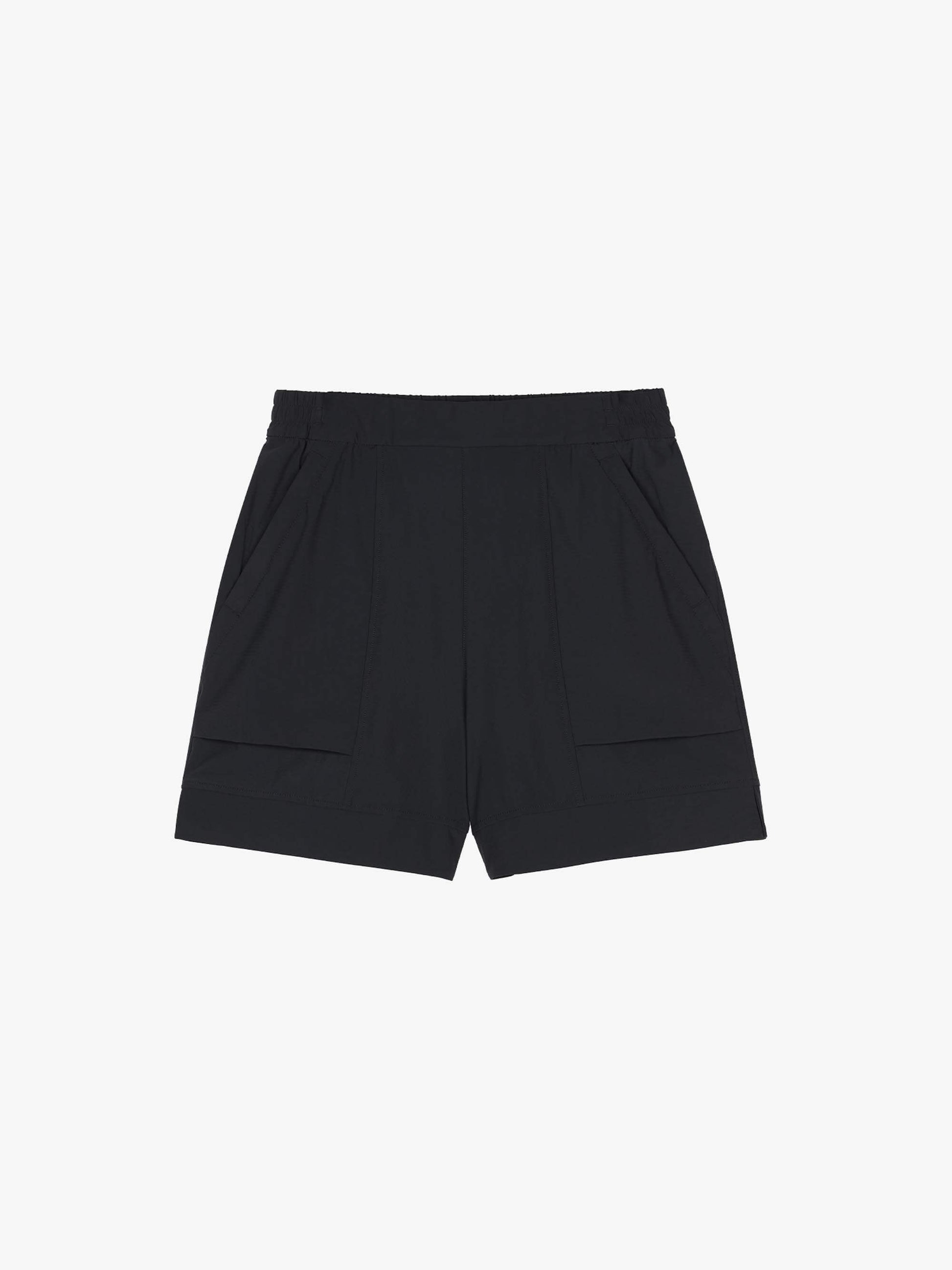 Flat lay of a pair of light black mid-waist shorts displayed on a plain background. The shorts feature an elastic waistband, side pockets, and a clean, minimalistic design.