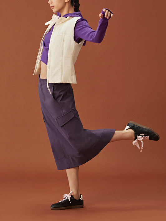 side of woman in purple hoodie, white vest and dark purple midi skirt.