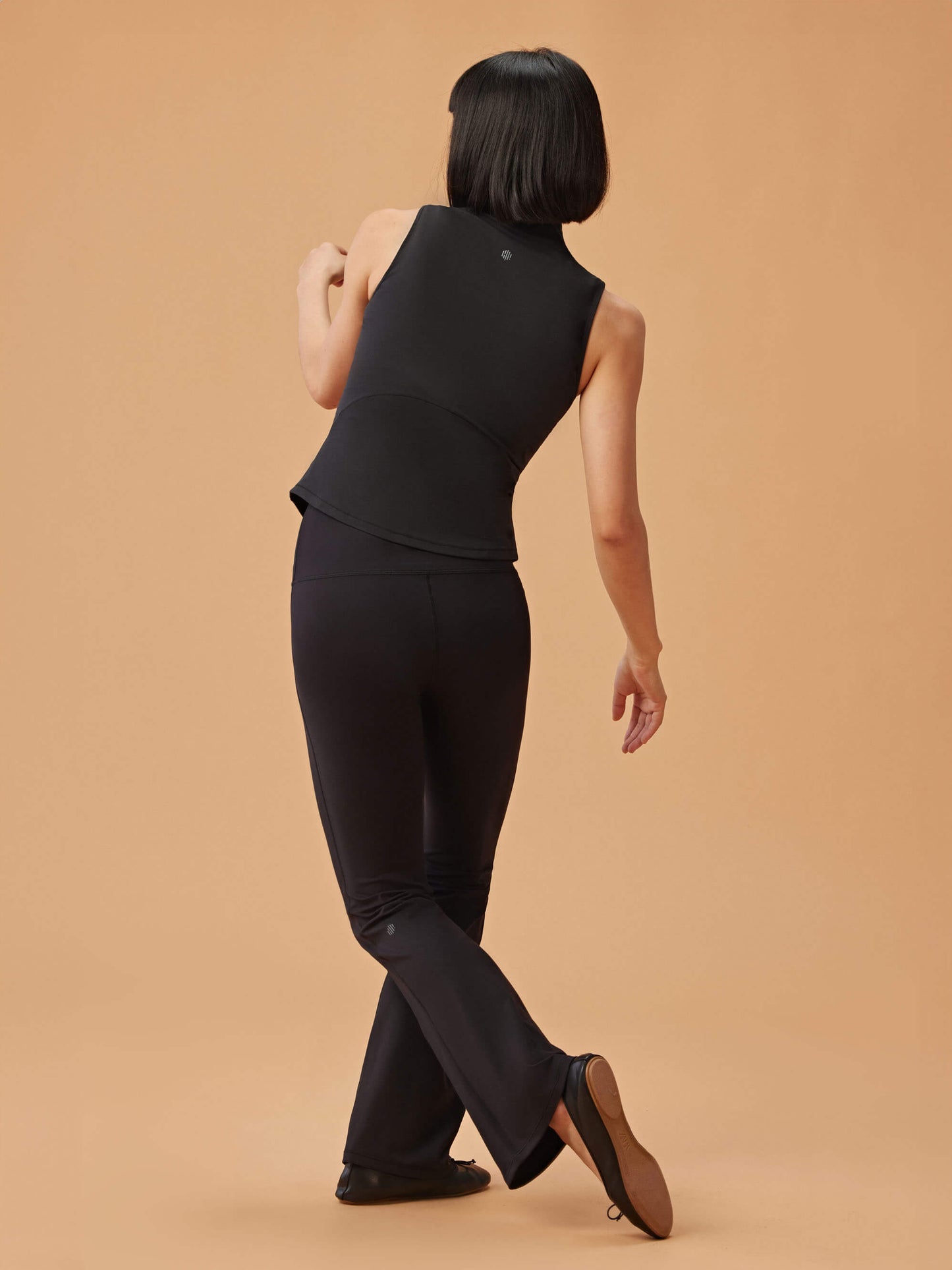 back of woman in black crew neck sleeveless top and black flare pants